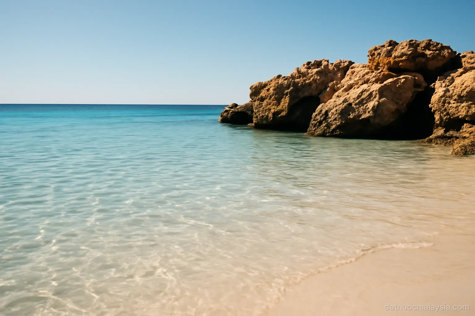 Clear shallow water over pale sand with a rocky outcrop nearby, bright midday sun, no boats